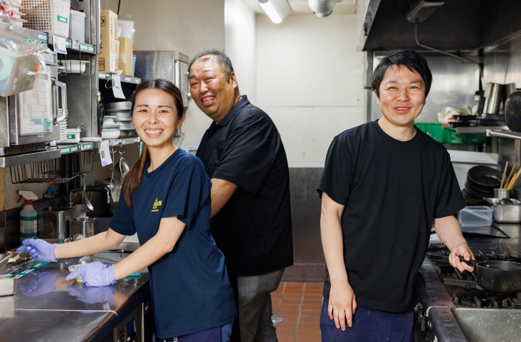 3人のキッチンスタッフが作業をしながら笑顔でカメラの方を向いている写真